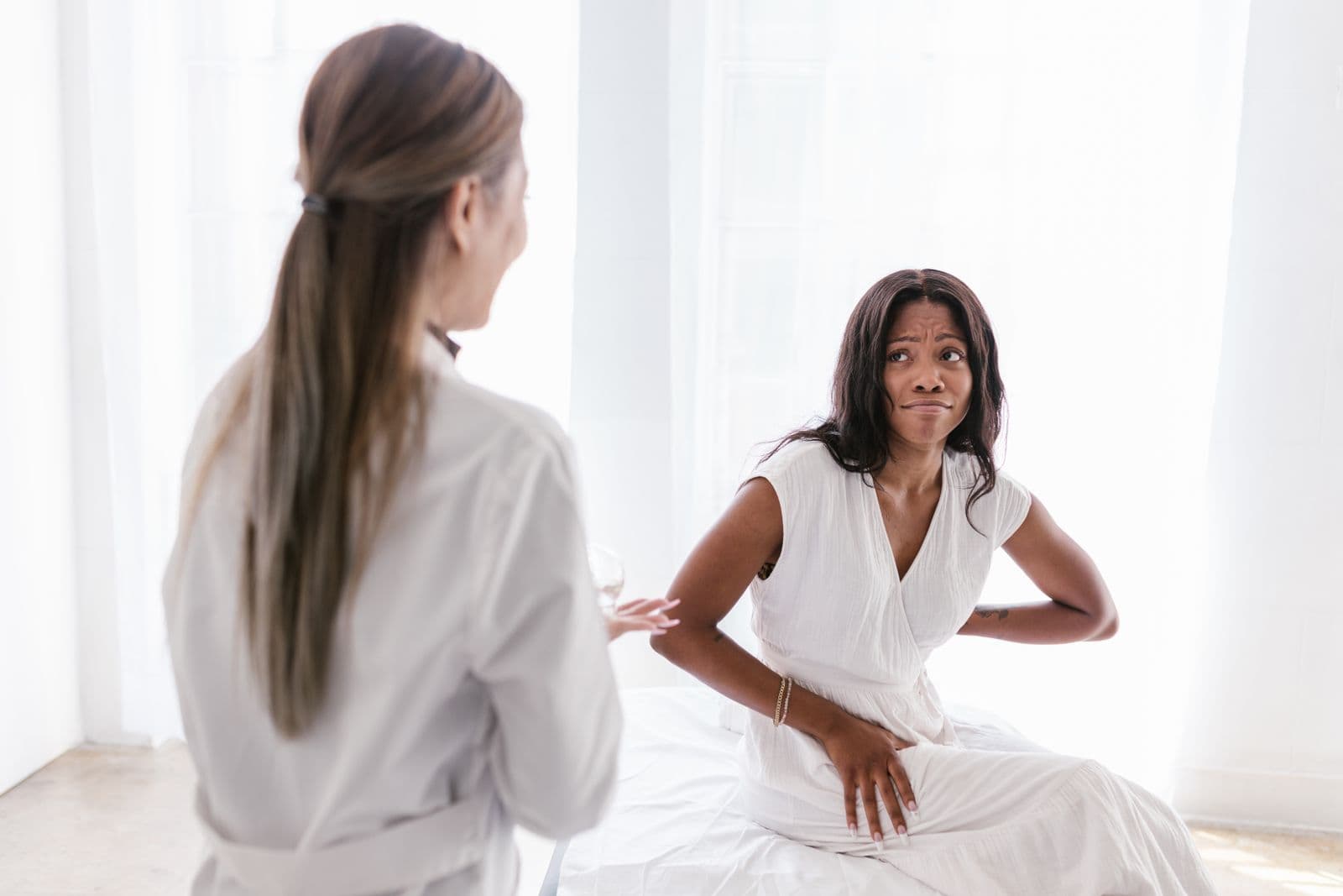 Woman holding her lower back while a clinician assesses her in a bright treatment room