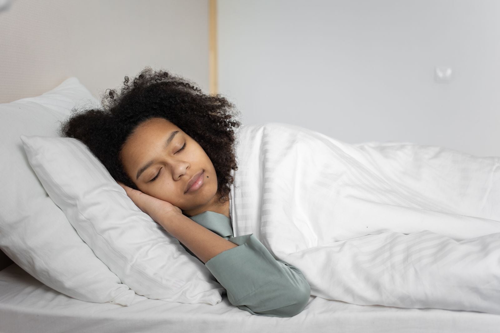 Woman sleeping on her side on white pillows in a bright bedroom