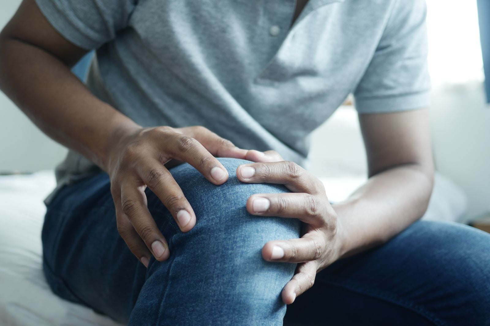 Close-up of a man in jeans holding his sore knee with both hands
