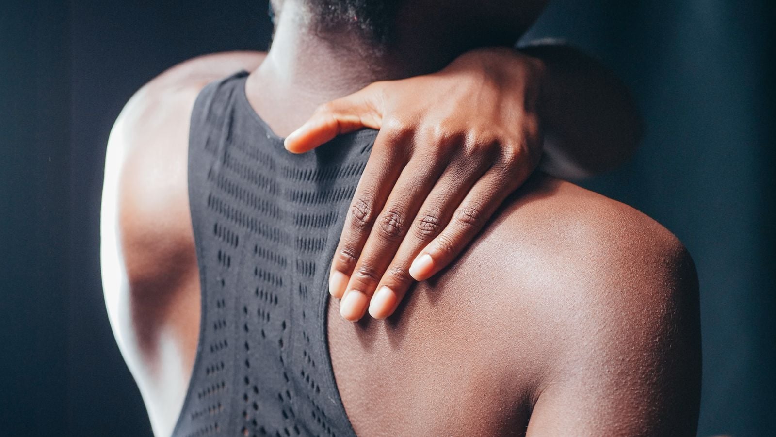 Close-up of a hand reaching over the shoulder to a tender spot on the upper back