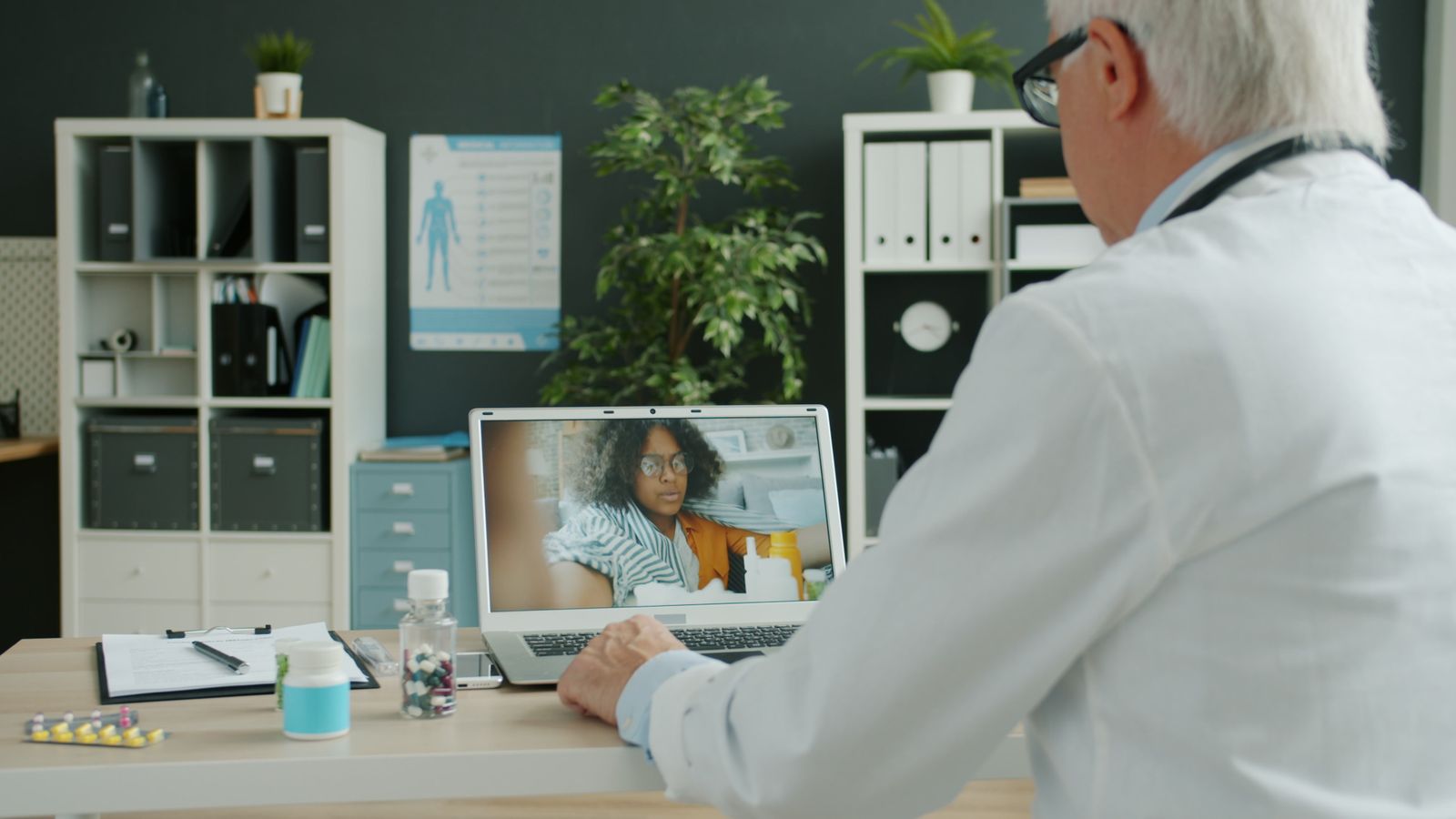 Clinician at a desk holding a video visit with a patient shown on a laptop