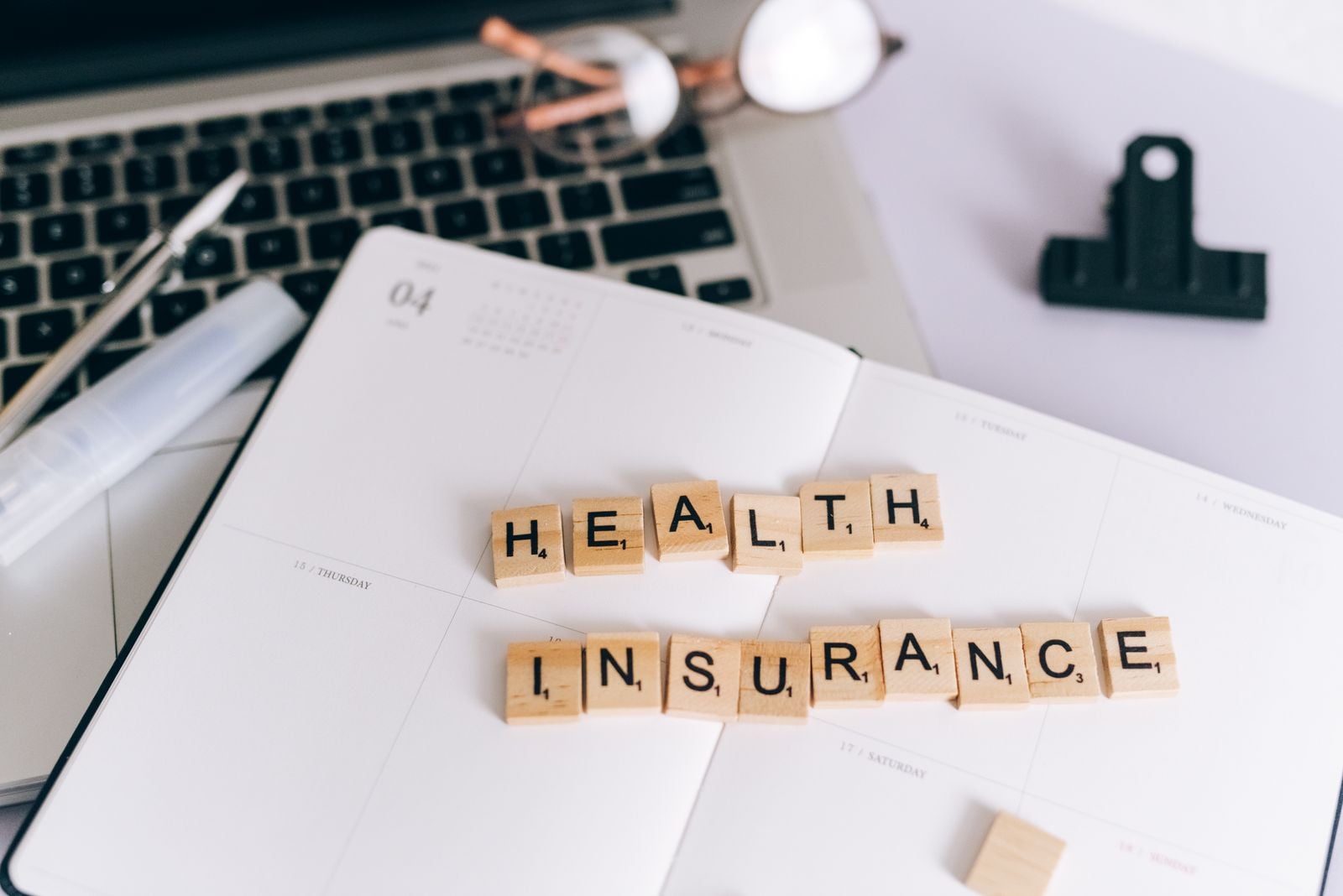 Letter tiles spelling 'Health Insurance' on an open planner beside a laptop