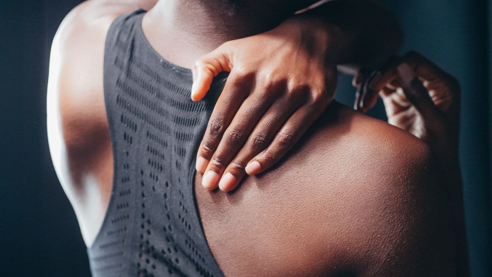 Close-up of a woman gripping the sore muscle between her neck and shoulder