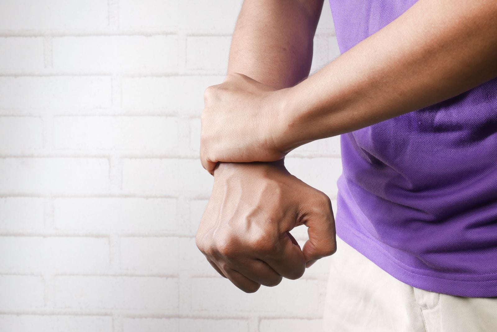 Man gripping his sore wrist against a white brick wall