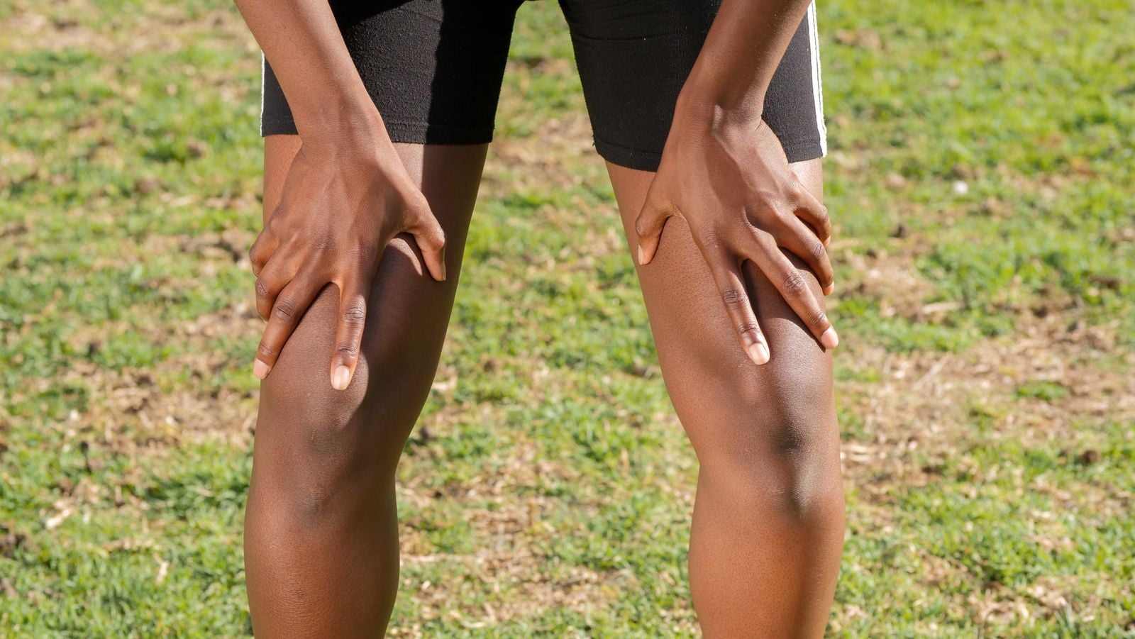 Person resting both hands on sore knees outdoors