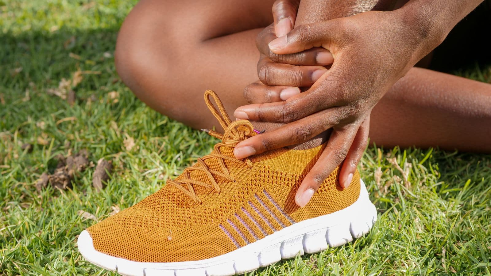 Runner sitting on the grass holding a sore ankle above a running shoe