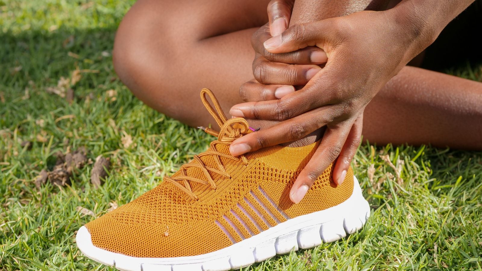 Runner sitting on the grass holding a sore ankle above a running shoe