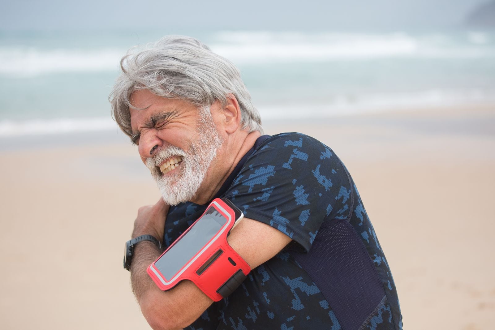 Man grimacing and holding his sore shoulder during a walk on the beach
