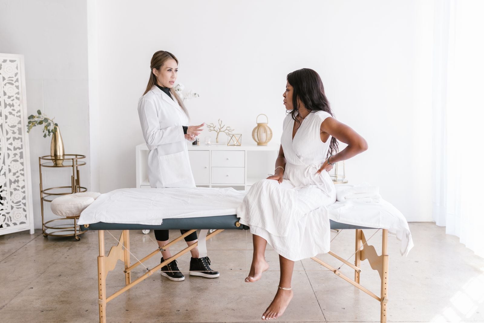 Clinician consulting a woman seated on a treatment table in a bright, airy treatment room