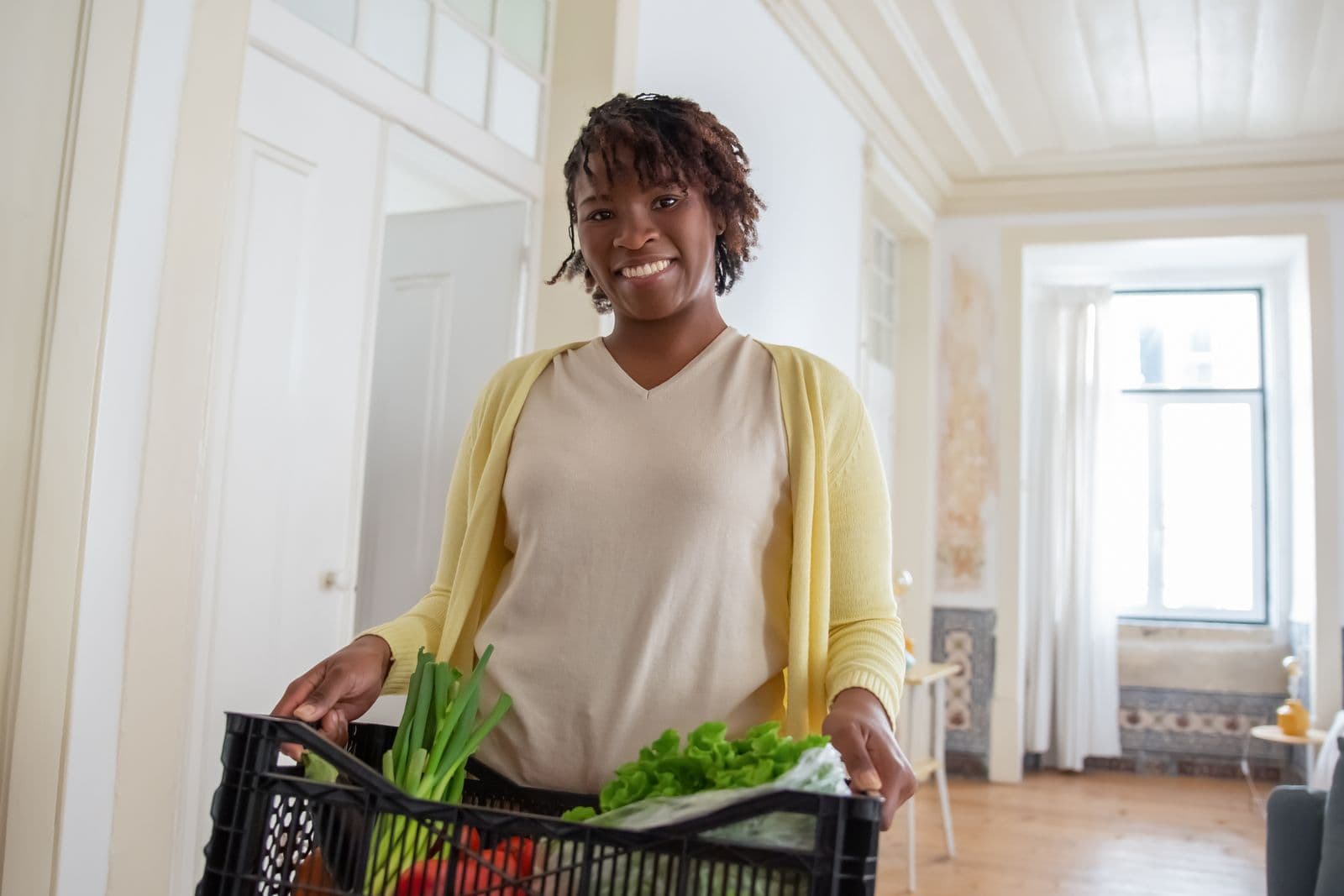 Smiling woman holding a crate of fresh vegetables and greens